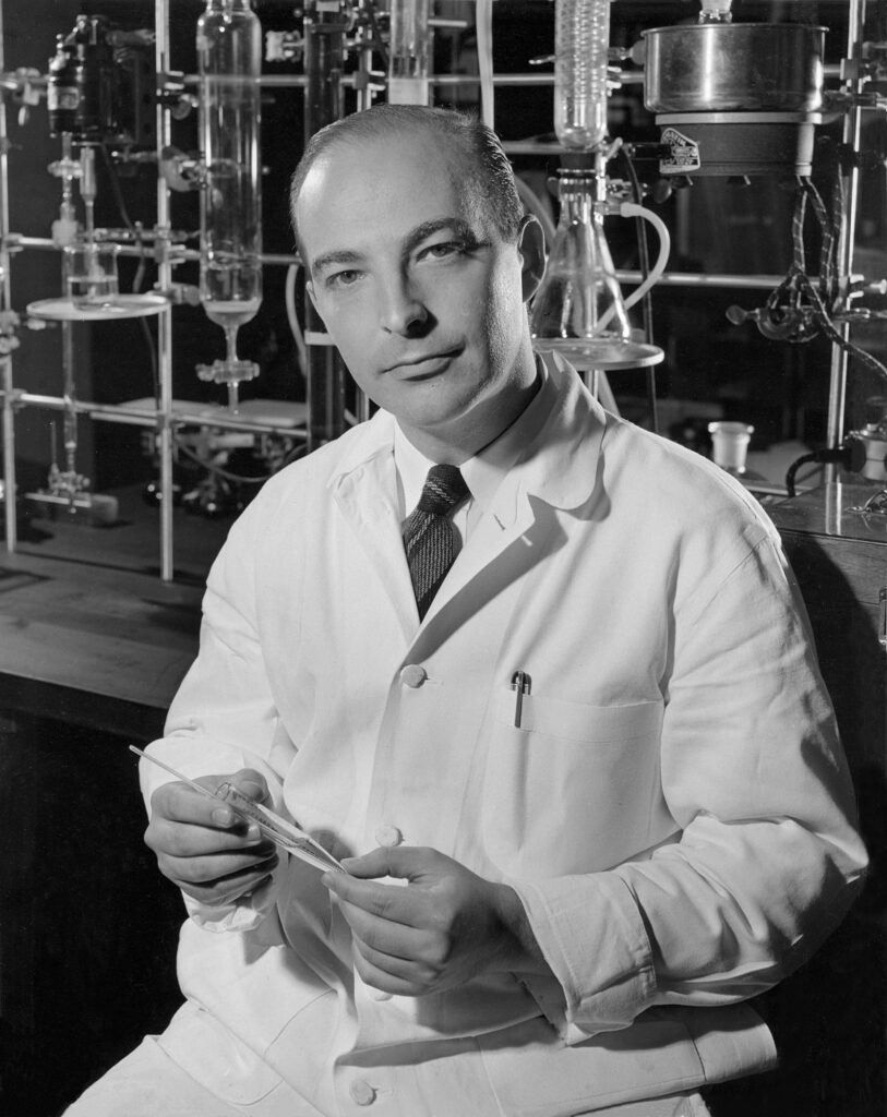 Man in lab coat sitting in front of lab glass equipment