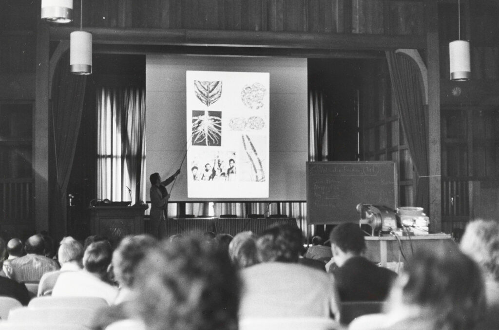 Man on stage talking in front of projected images