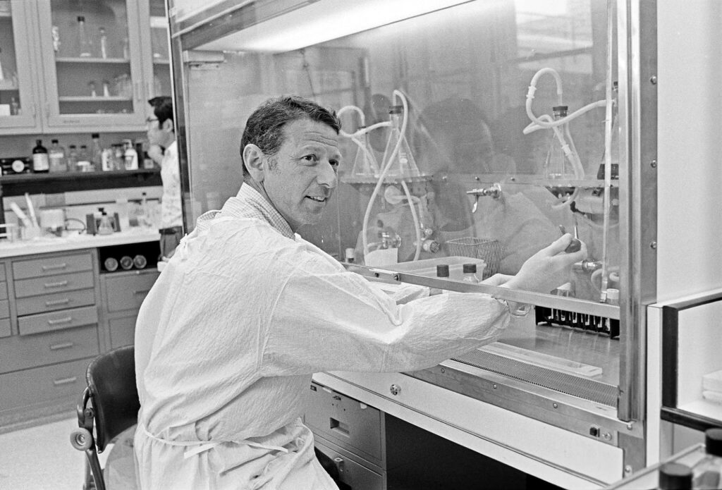 Man in lab smock and gloves working under a hood