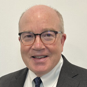 Sam Tharpe, smiling, in glasses and suit with tie